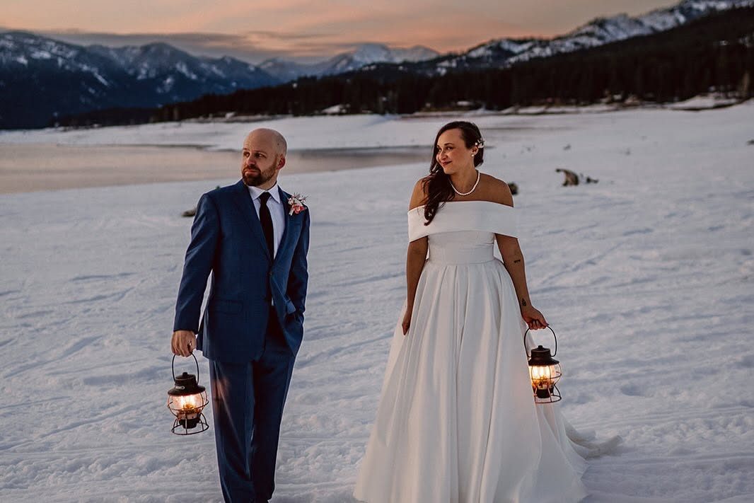 Amanda and Jordan on their wedding day, walking a snowy beach at sunset with lanterns