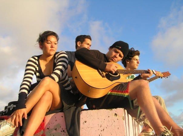 Jordan playing acoustic guitar with friends on a rooftop at sunset
