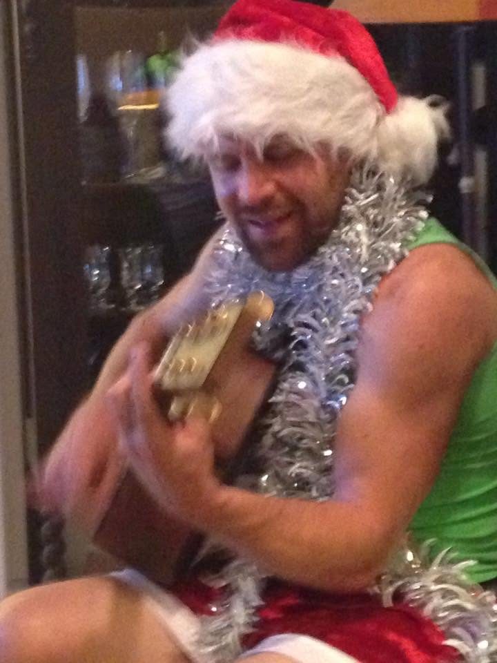 Jordan in a Santa hat and tinsel playing guitar at a holiday party