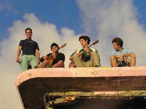 Jordan playing guitar with three friends atop a concrete ledge