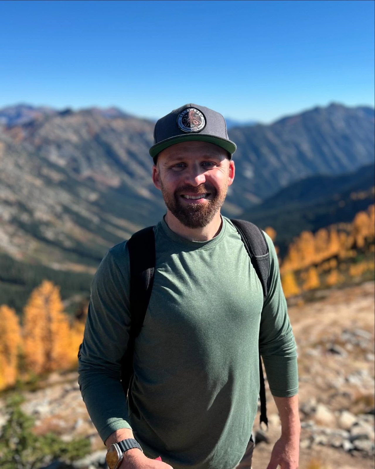 Jordan wearing a Salty Crew hat on a mountain hike among golden larch trees